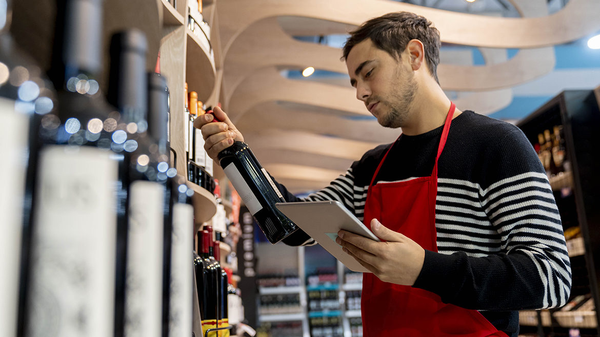 man preparing an online order holding a tablet and looking at the wine brand at the supermarket