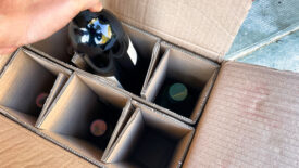 a person is taking a bottle of wine ordered on the internet out of a delivery box