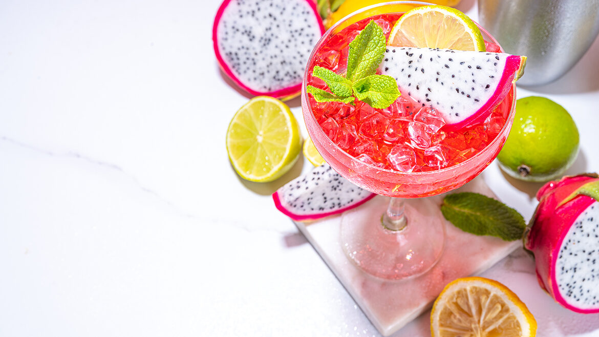 Sweet colorful tropical cocktail with pitaya or dragon fruit, lime and mint. Martini alcohol pitahaya fruit drink over light tile background copy space