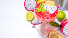 Sweet colorful tropical cocktail with pitaya or dragon fruit, lime and mint. Martini alcohol pitahaya fruit drink over light tile background copy space